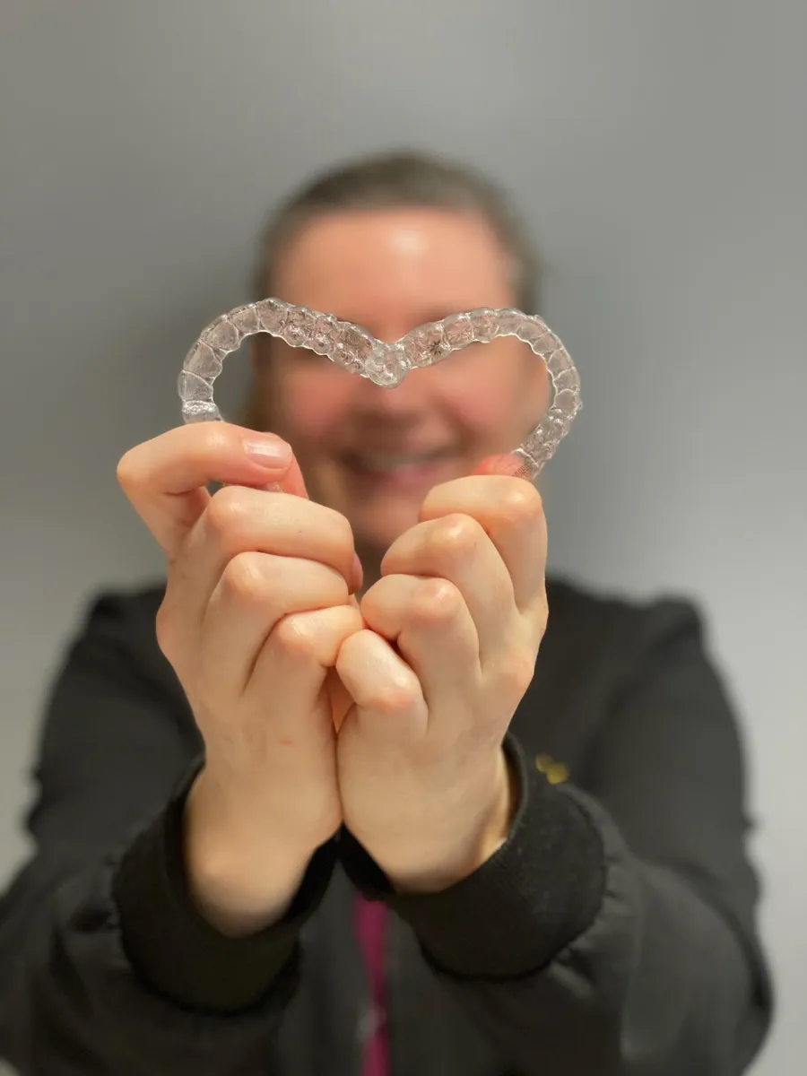 Smiling patient holding two clear aligner trays in the shape of a heart