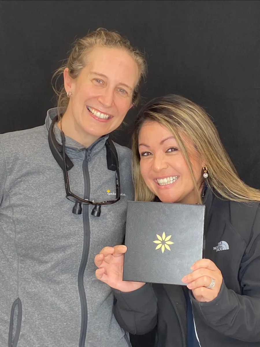 Smiling patient holding a Sunshine Dentists gift box beside a dental team member in Burke, VA